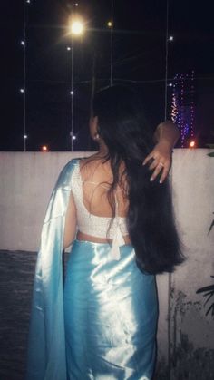 a woman with long hair standing in front of a wall at night wearing a blue skirt