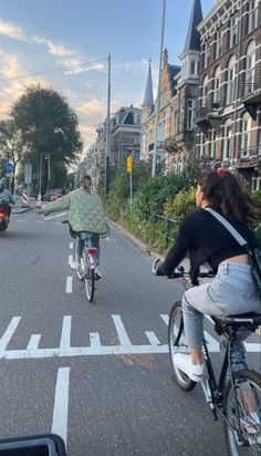 two people riding bikes down the street in front of some buildings and cars on it