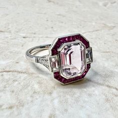 Breathtaking handcrafted platinum Art Deco style kunzite, ruby and diamond halo cocktail/engagement ring! It is set with a fine emerald cut kunzite weighing 4 carats (10.05 x 7.64 mm). It is haloed by a row of natural French cut ruby weighing approximately 1/2 carat. It is accented by 2 baguette diamonds and 6 old European cut diamonds weighing approximately 0.40 carat. Fine milgrain adds to the delicacy of the ring. Beautiful openwork filigree decorate the under gallery. The ring measures 14.56 Art Deco Ruby Ring, Diamond Halo Ring, French Cut, Baguette Diamonds, Halo Diamond Ring, Ruby Diamond, Halo Ring, Halo Rings, Ruby Ring