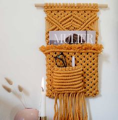 a macrame wall hanging with eyeglasses on it and a candle next to it