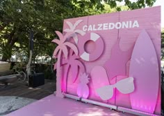 a pink sign that says caledonia with palm trees and surfboards on it