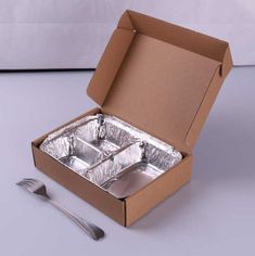 an open cardboard box with silverware in it on a white surface next to a fork and spoon