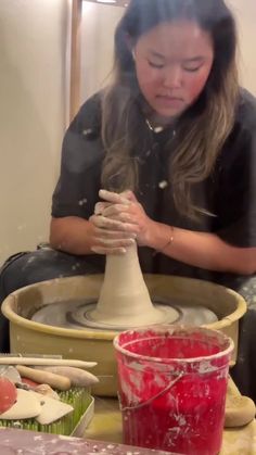 a woman sitting at a table working on a pottery wheel and making something out of clay