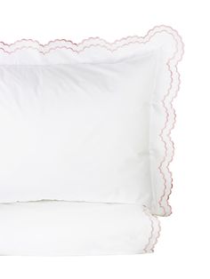 a white pillow with scalloped edges and pink piping on the side, sitting next to two pillows