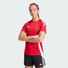 a woman in red shirt and black shorts standing with her arms crossed, looking at the camera