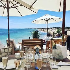 an outdoor dining area with tables and umbrellas on the beach, overlooking the ocean