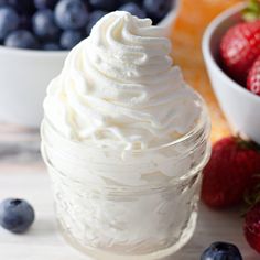 whipped cream in a jar surrounded by fresh berries and blueberries on a table top