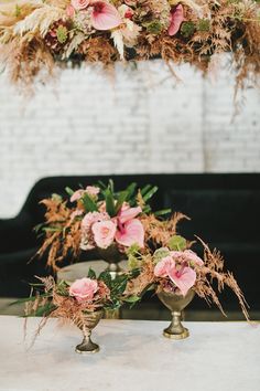 two vases filled with flowers sitting on top of a white table next to a black couch