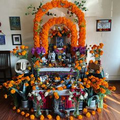 an altar with orange flowers and pictures on the wall behind it, surrounded by potted plants