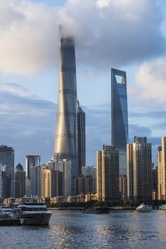 a large city with tall buildings and boats in the water next to it on a cloudy day