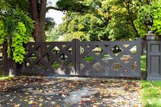 an open gate in the middle of a park with leaves on the ground and trees around it