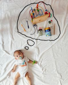 a baby laying on top of a bed with toys in the shape of a thought bubble