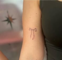 a woman's arm with a bow tattoo on the left side of her arm