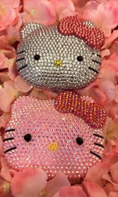 two hello kitty sequins laying on top of pink flowers with one wearing a bow