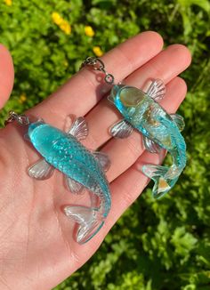 two small glass fish on a chain in someone's hand