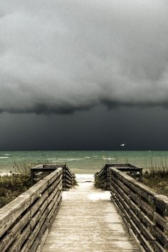 a wooden walkway leading to the beach with storm clouds in the sky over the ocean