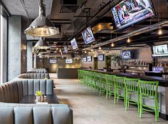 a sports bar with green chairs and televisions on the wall above it's windows