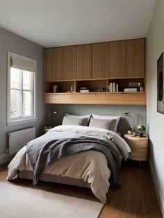 a bed sitting under a window next to a wooden shelf filled with books and pillows