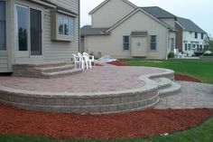 a brick patio with steps and chairs in front of the house on a sunny day