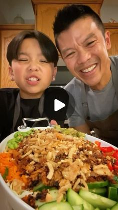 a man and boy are smiling in front of a large bowl of food with vegetables