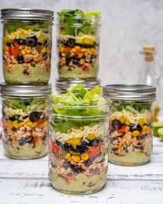 four mason jars filled with salads on top of a white table