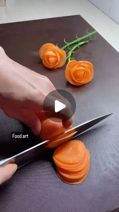 a person cutting carrots with a knife on top of a table next to flowers