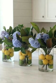 three vases with lemons and blue flowers in them on a countertop next to cabinets