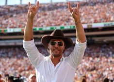 a man with his hands up in the air at a football game while wearing a hat and sunglasses