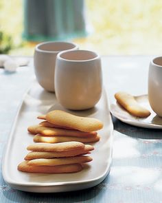 some cookies are on a white plate with two cups and saucers next to them