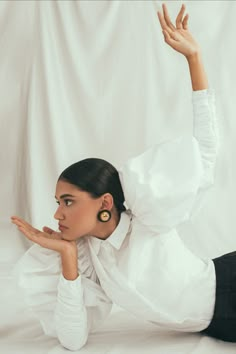 a woman in white shirt and black pants laying on the ground with her hand up