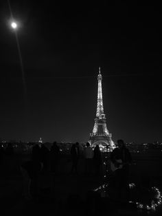 the eiffel tower lit up at night in black and white with people looking on