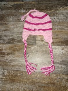 a crocheted hat with pink and white stripes on it sitting on top of a wooden floor