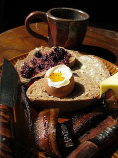 an egg is sitting on top of bread with butter and jam next to some bacon