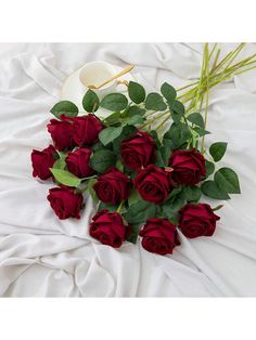 a bunch of red roses laying on top of a white blanket next to a cup