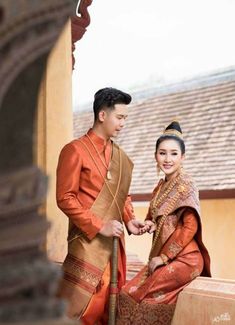 a man and woman dressed in traditional thai garb standing next to each other on a balcony