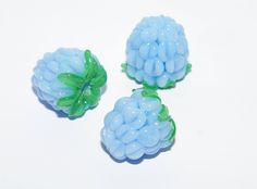 three blue beads with green leaves are on a white surface, and one is in the shape of a flower