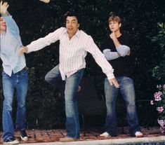 three men are playing frisbee by the pool in front of some trees and bushes