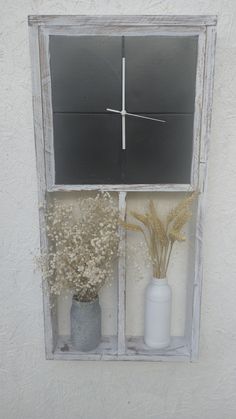 two vases with dried flowers sit in front of a clock on a window sill