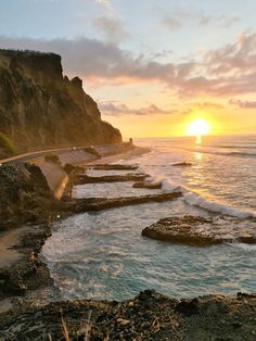 the sun is setting over the ocean and rocky shore