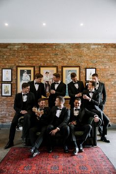 a group of men in tuxedos are sitting on a couch and drinking wine