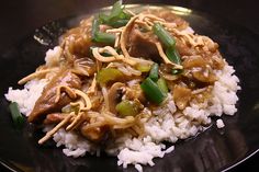 chinese pork chow mein with rice and green onions on a black plate in a restaurant