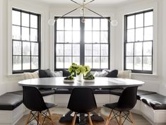 a dining room table with four chairs and a bench in front of two large windows