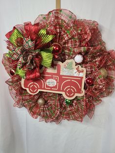 a christmas wreath with a red truck and green bow hanging on the front of it