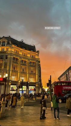 people walking on the sidewalk in front of a building at dusk with an orange sky