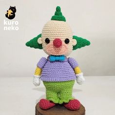 a crocheted clown doll sitting on top of a piece of wood