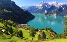 a lake surrounded by mountains and green grass