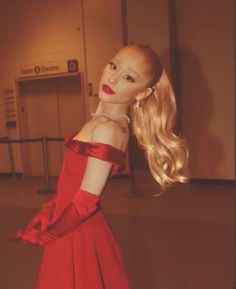 a woman in a red dress with long blonde hair and gloves on her shoulder, posing for the camera