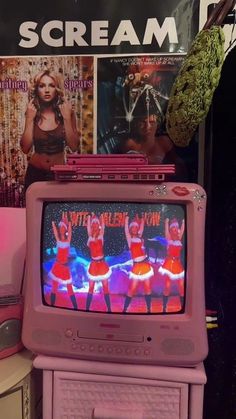 an old pink tv sitting on top of a table next to a wall covered in posters