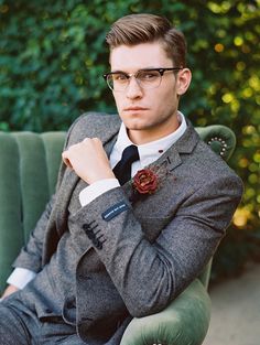 a man wearing glasses and a suit sitting on a green chair with his arms crossed