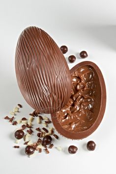 an egg shell filled with chocolate and nuts on a white surface next to pieces of chocolate